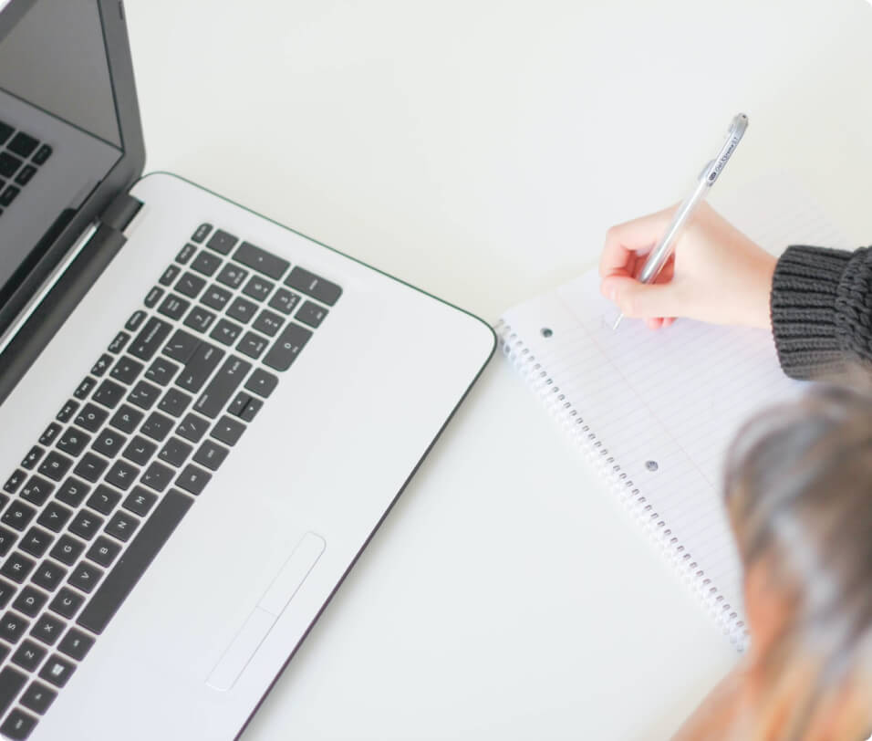 A person writing on a notebook next to a laptop for On-Page SEO Services.