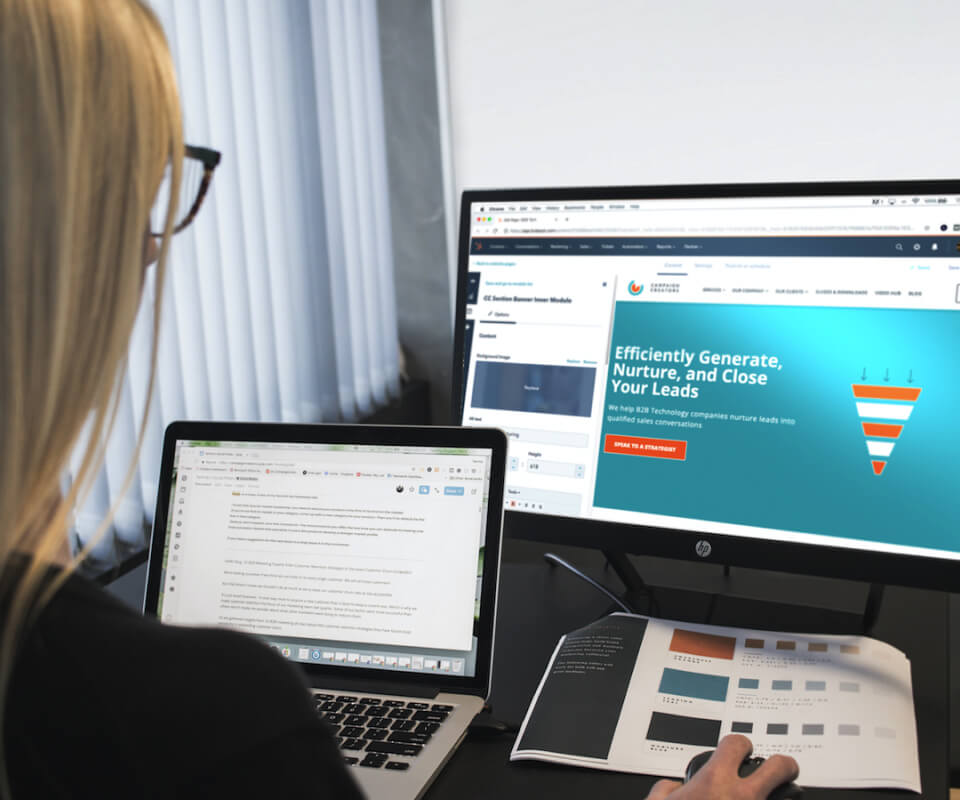 A woman is sitting at a desk with a laptop, designing an infographic.