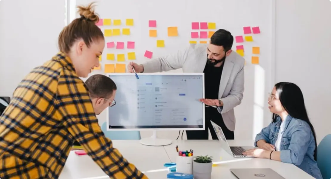 Team collaborating during a presentation, with sticky notes on the wall and a screen displaying data.