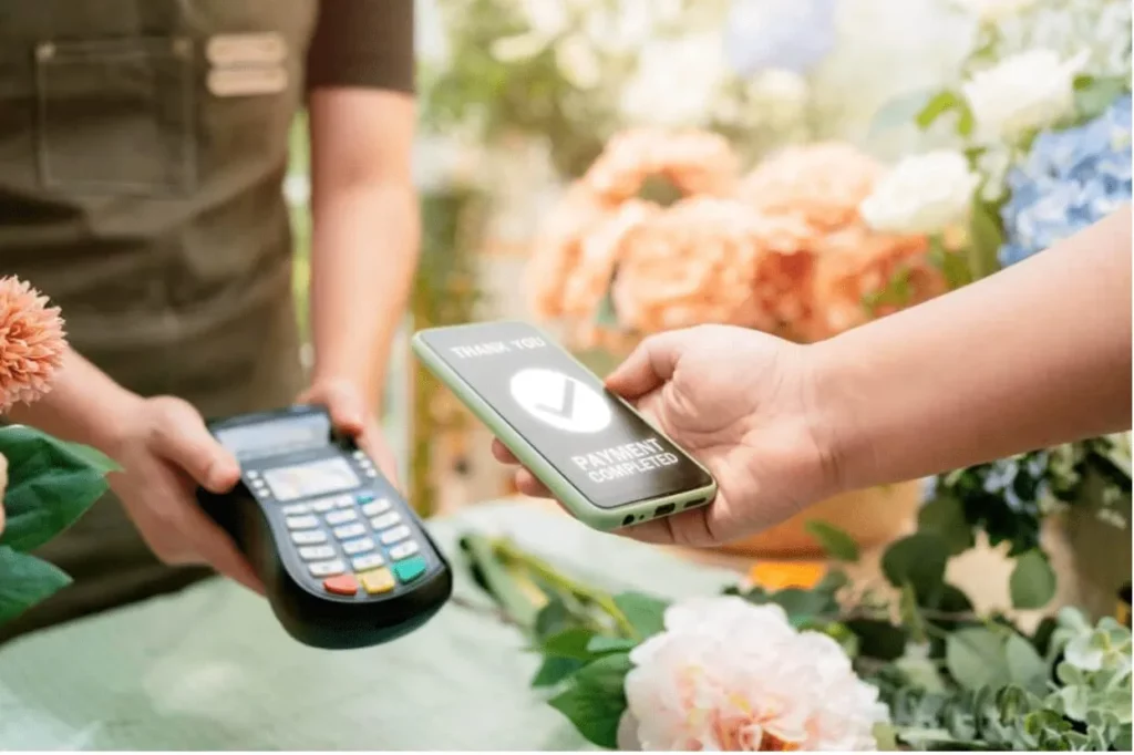 Customer completing a contactless payment using a smartphone at a flower shop counter, with a digital confirmation message reading 